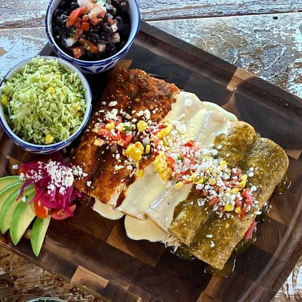 A plate of enchiladas from Mexican Sugar, displaying red, white, and green sauces alongside rice and beans, highlighting the colorful and appetizing presentation of their dishes.