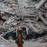 Rescue worker walking past a car buried under rubble in Mexico City after the devastating earthquake.