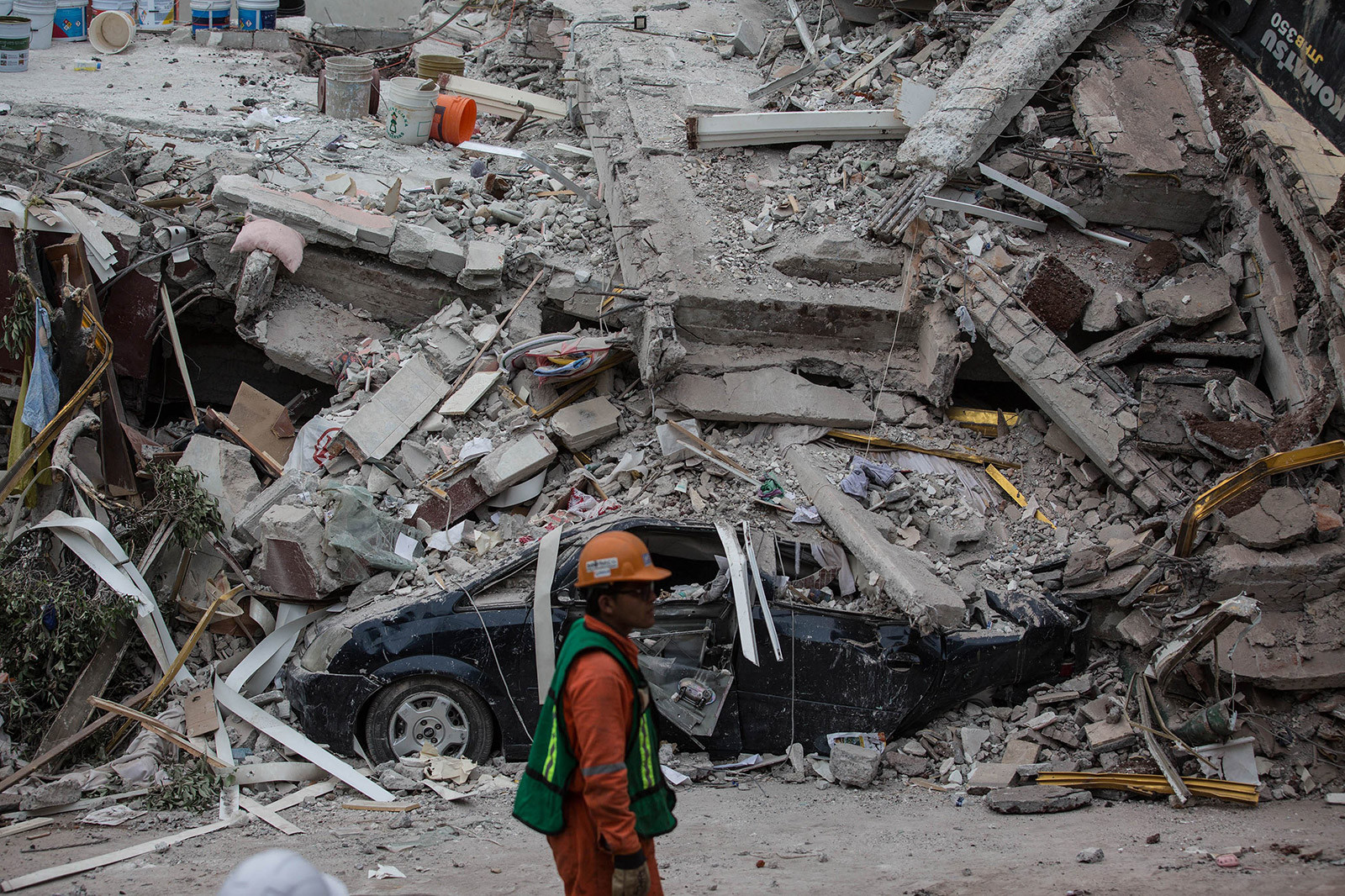 Rescue worker walking past a car buried under rubble in Mexico City after the devastating earthquake.