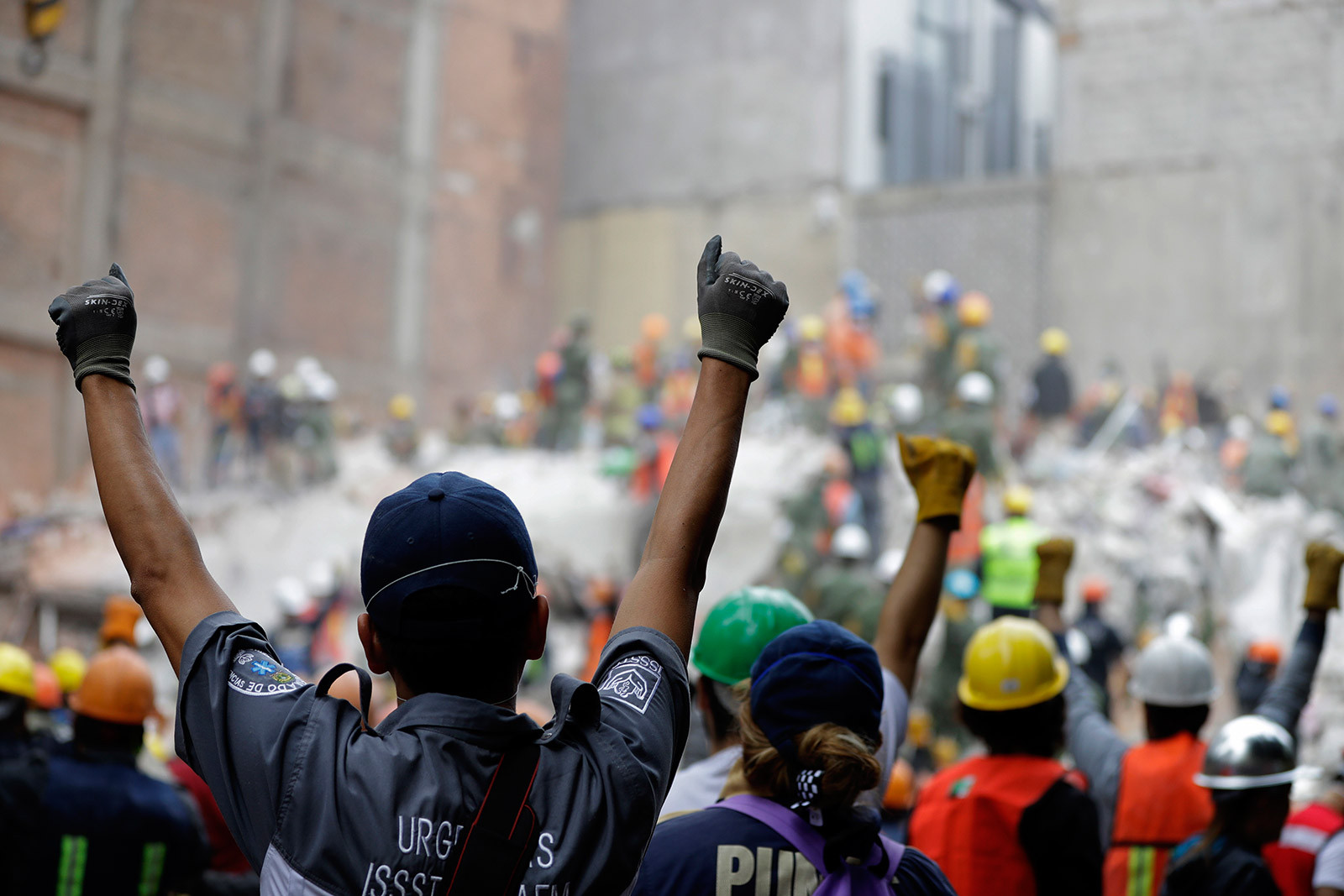 Rescuers hold up closed fists, signaling for silence as they search for survivors in a flattened building in Mexico City after the 2017 earthquake.