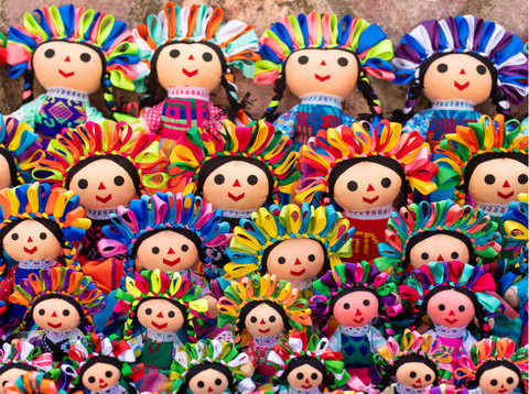 A close-up of a Lelé doll's face, showcasing its embroidered smile and colorful ribbons