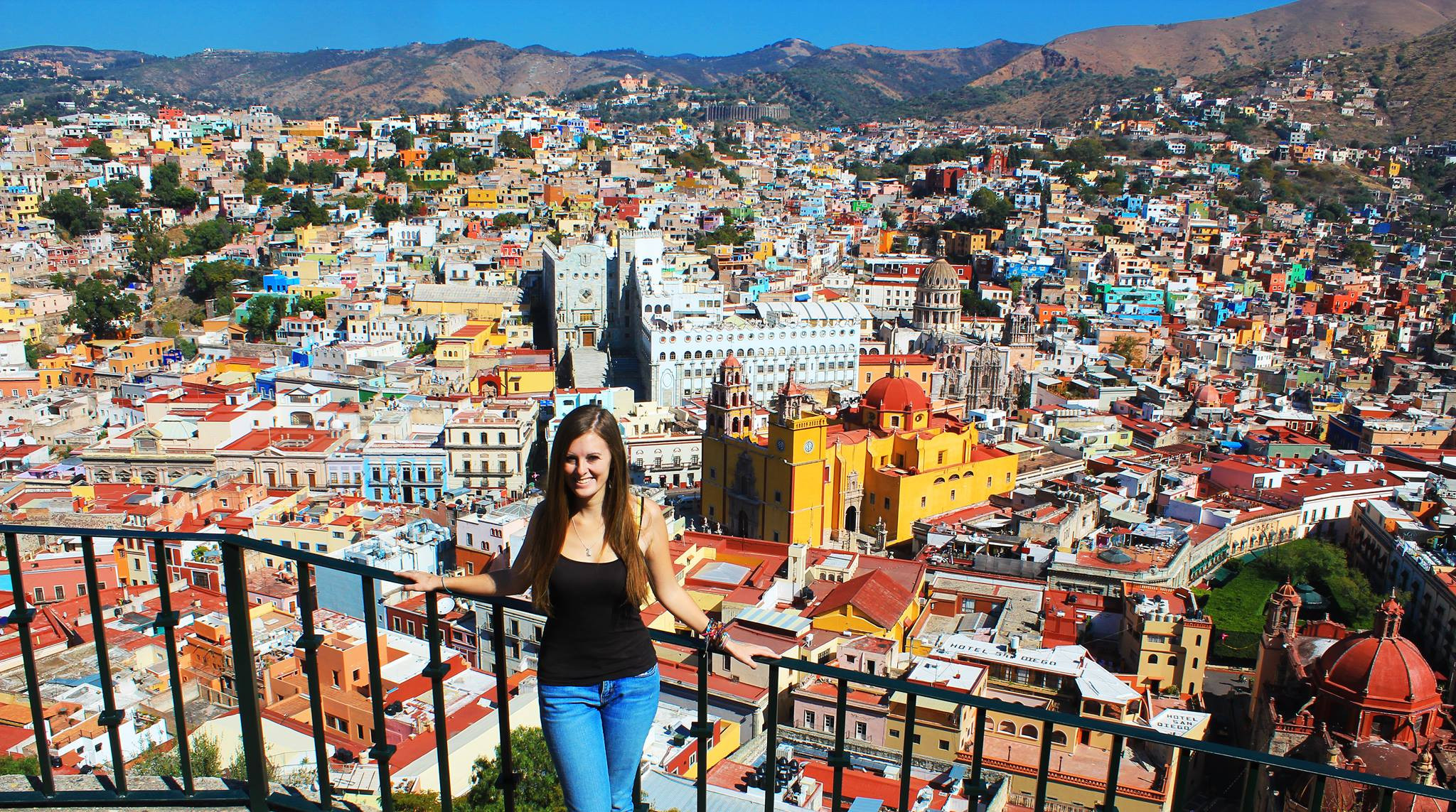 A woman standing on a viewpoint overlooking the colorful cityscape of Guanajuato, Mexico.