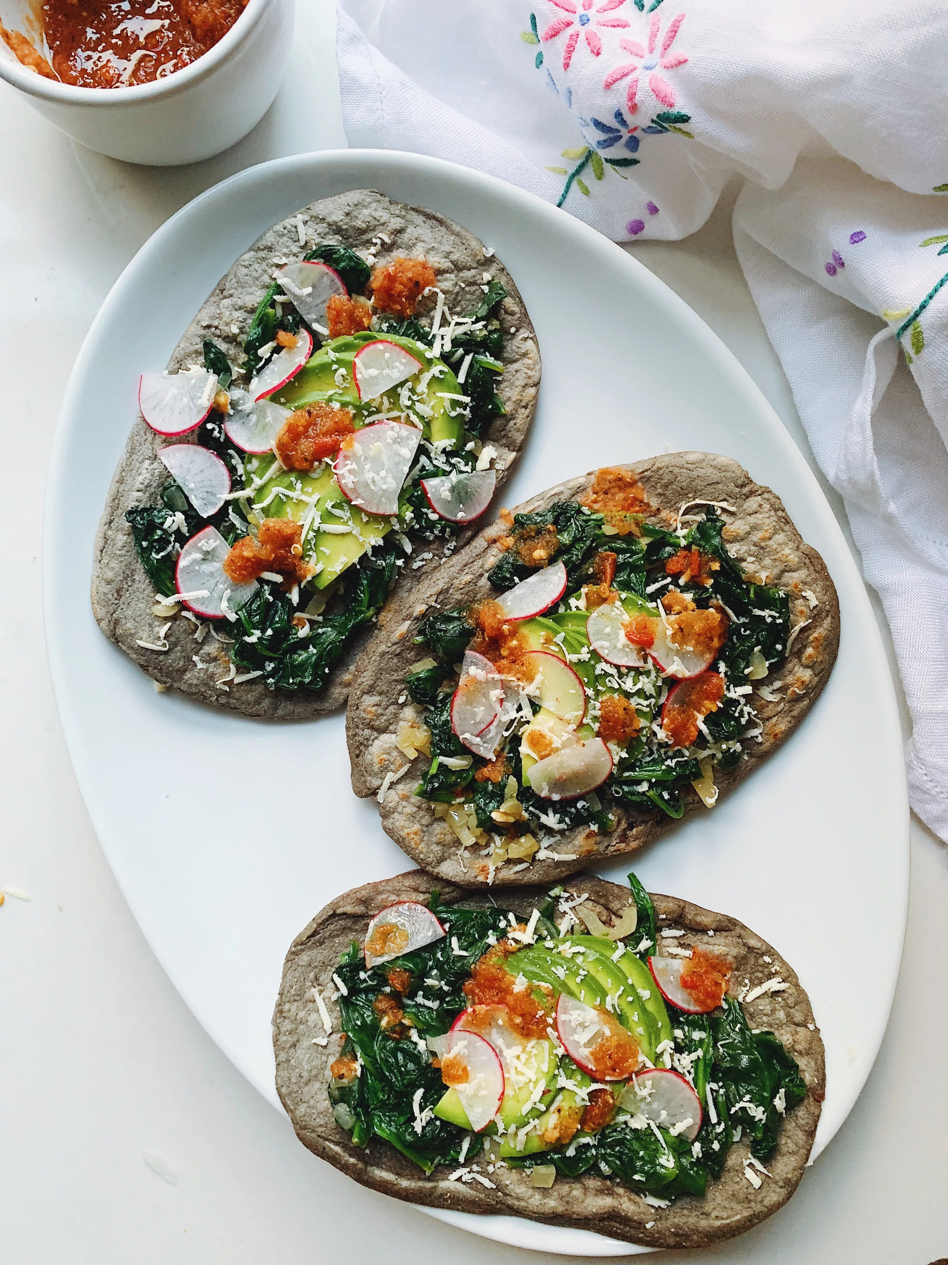 Close-up shot of a spinach huarache topped with fresh ingredients, showcasing the texture of the masa and the vibrant colors of the toppings.