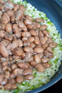 Adding drained pinto beans to the skillet with onions and jalapeño
