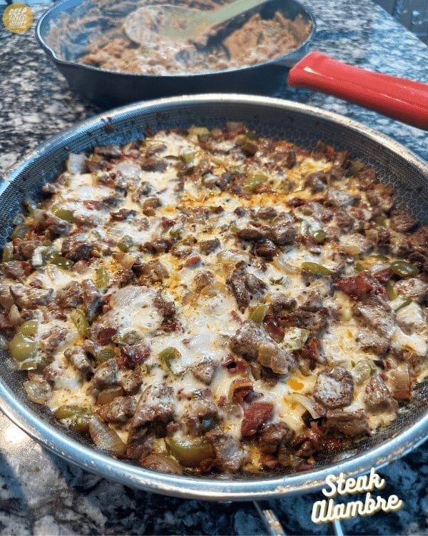 Authentic and delicious Alambre Mexican food featuring seasoned steak, bacon, and vegetables in a skillet.
