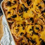 flat lay shot of a 9x13 filled with cheesy capirotada (mexican bread pudding) on a wooden table.