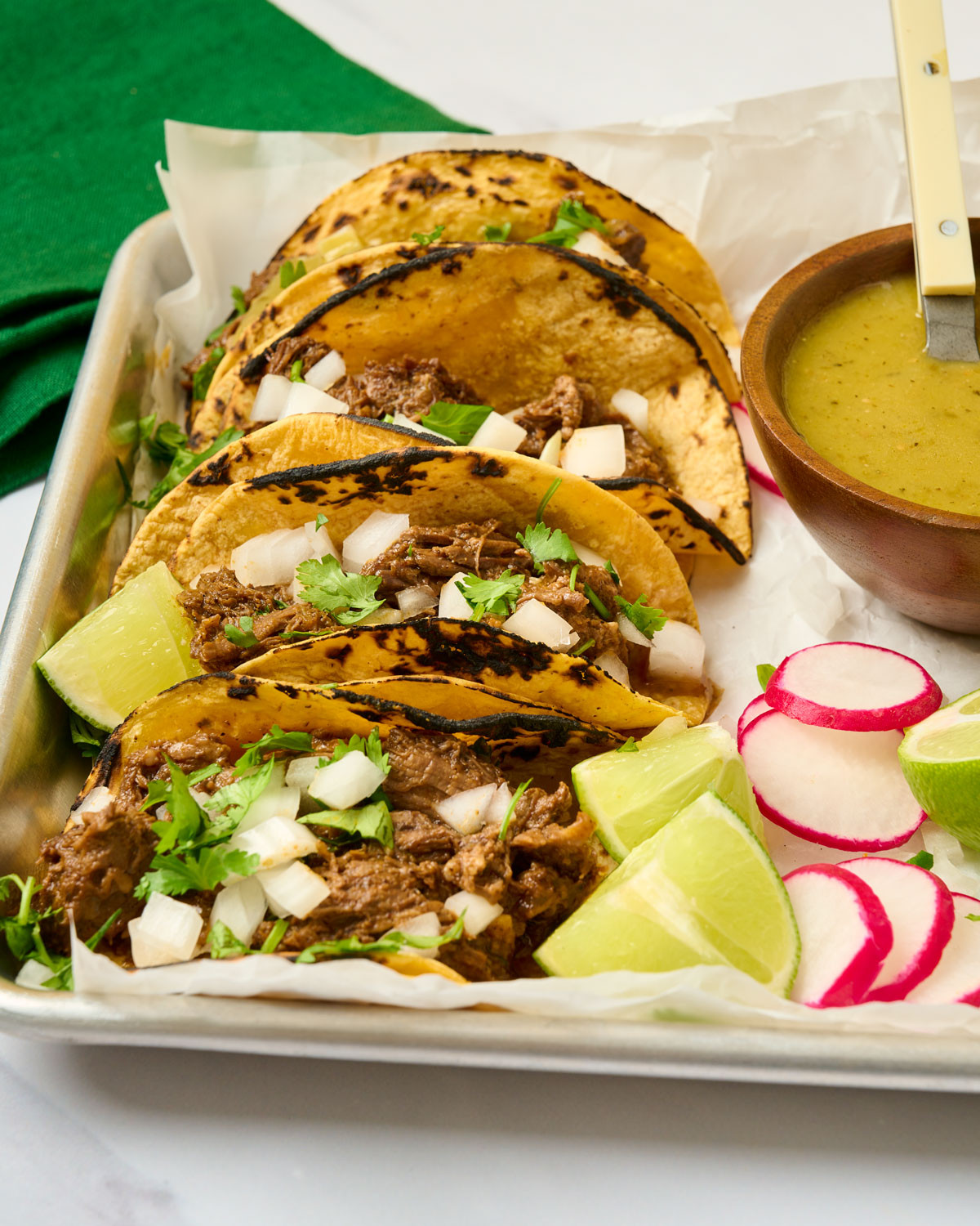 Angled view of barbacoa street tacos topped with cilantro and white onion, highlighting a popular Mexican meat dish.