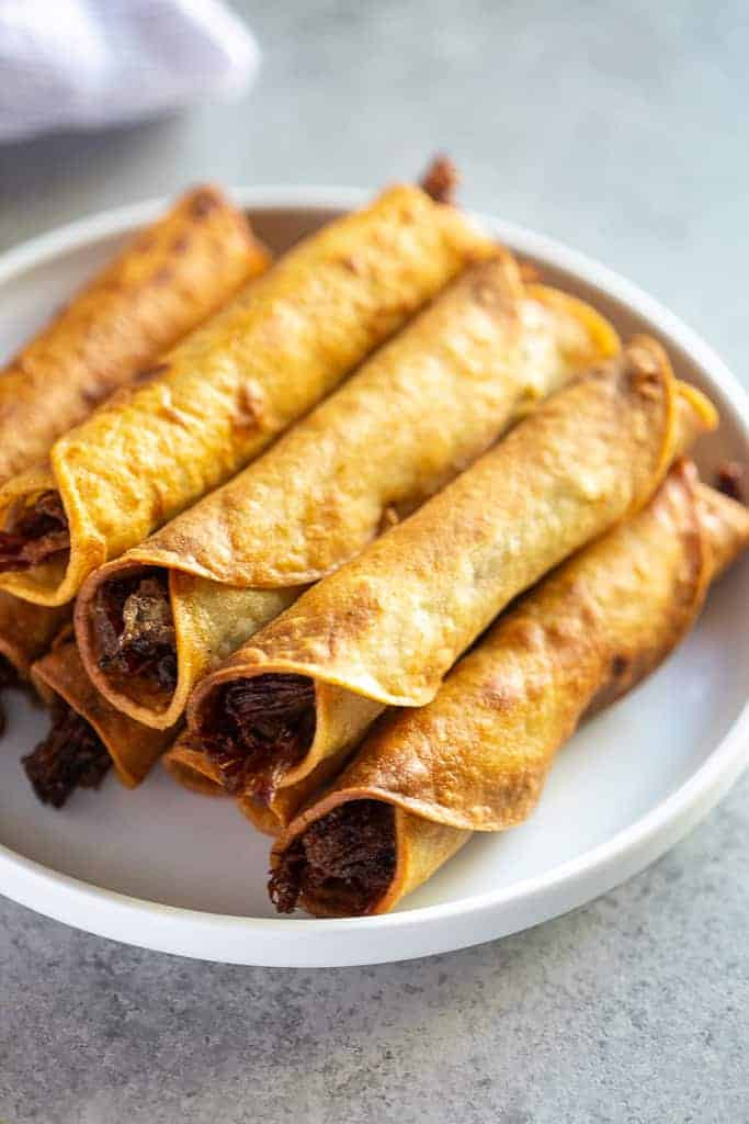 A plate of freshly baked homemade Mexican taquitos, stacked and ready to be served, showcasing a healthier cooking option.