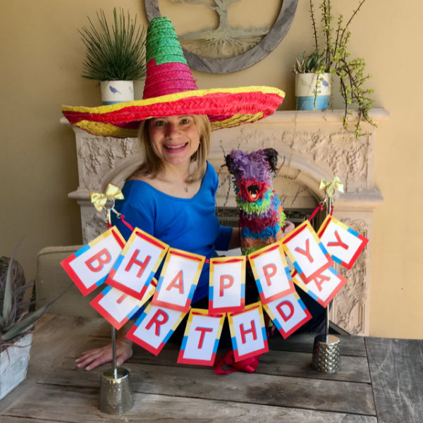 Woman smiling next to a large, vibrant birthday centerpiece, perfect for a Mexican fiesta theme.