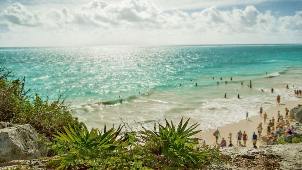 A crowded beach in Tulum, Mexico, on a sunny day, showcasing the town's Mayan ruins and tourist-friendly zones for safe exploration