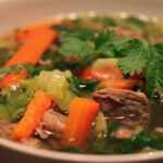 Hearty Caldo de Res served in a bowl with cilantro and lime garnish