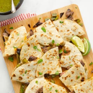 A close up featured image of layers of quartered carne asada quesadillas on a cutting board.