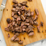 Slices of carne asada steak, cubed and piled on a cutting board.