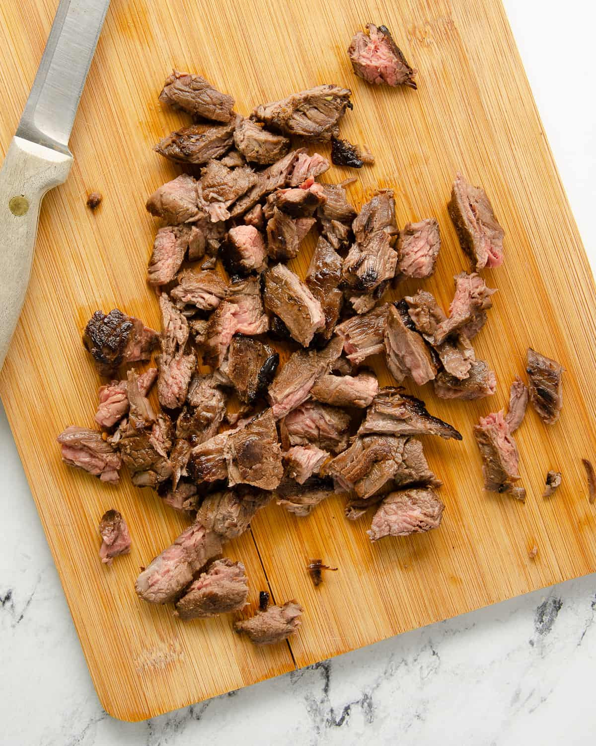 Slices of carne asada steak, cubed and piled on a cutting board.