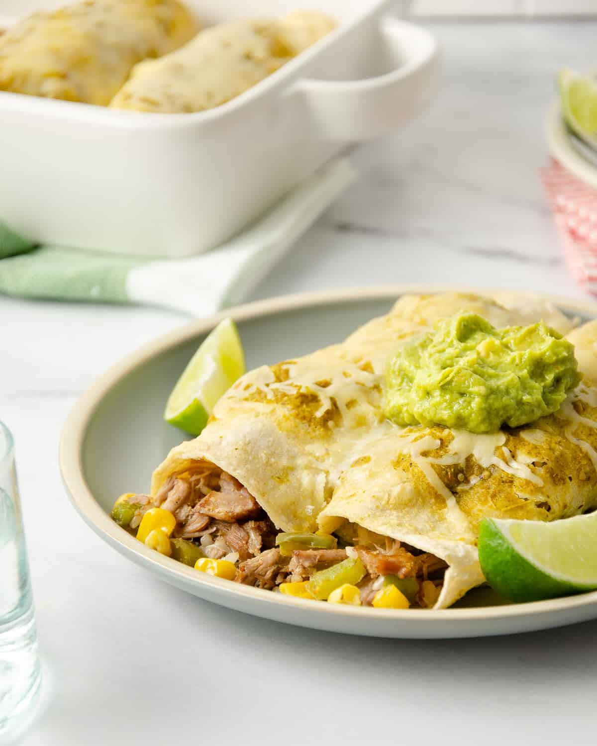 Two enchiladas on a plate topped with cheese and guacamole, featuring carnitas as the Mexican meat filling.