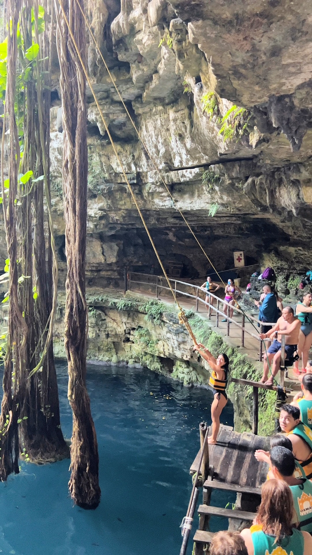 Person swimming in the crystal clear turquoise waters of Cenote Oxman, surrounded by hanging vines