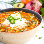 Mexican soup bowl brimming with colorful toppings like tomatoes, avocado, and jalapeño, ready to customize.