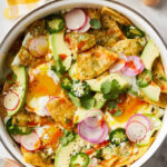 Serving of chilaquiles with fried eggs, crema, and fresh toppings.