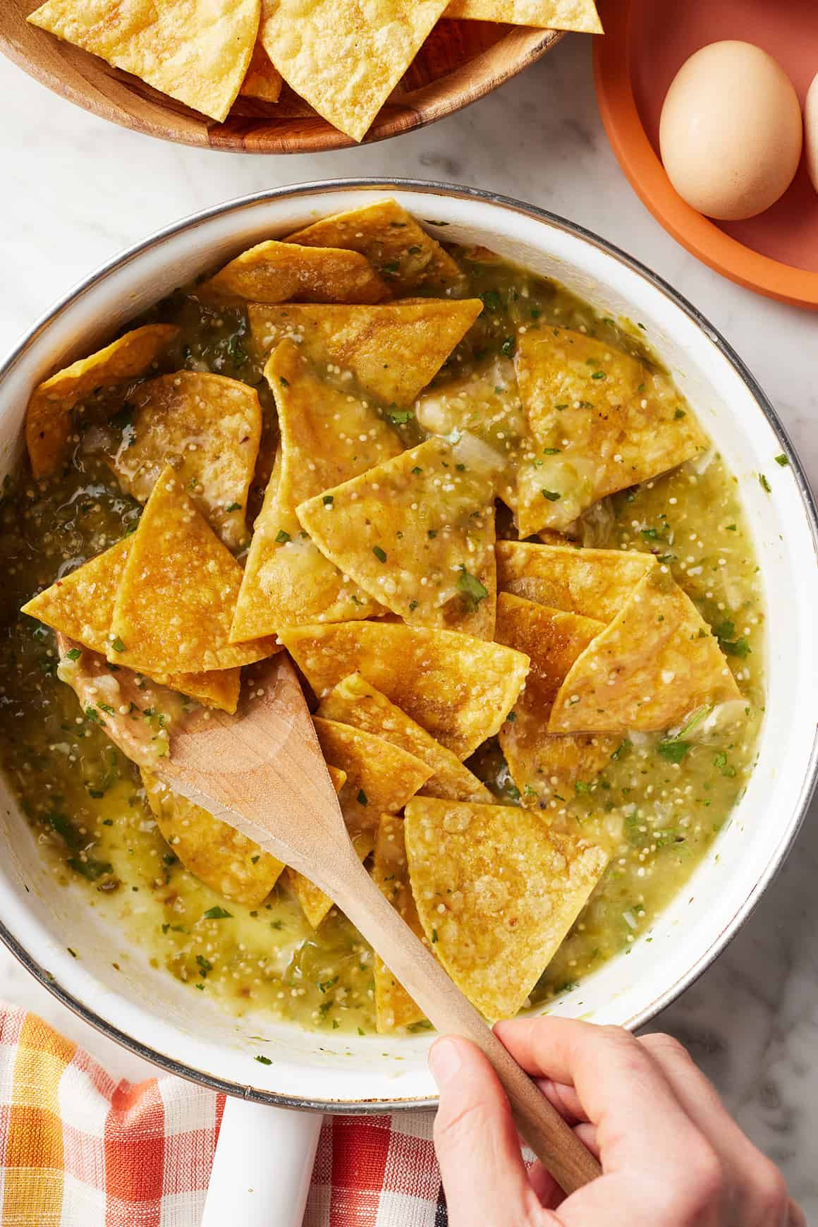 Close-up of chilaquiles verdes being stirred in a skillet, showing the salsa-coated chips.