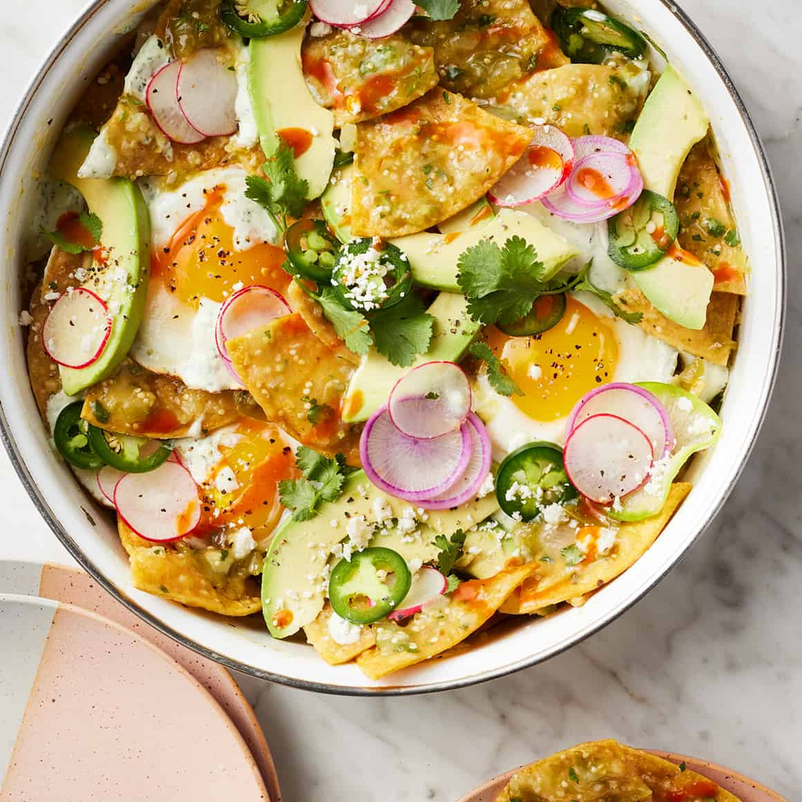 Overhead view of a serving of chilaquiles in a bowl, garnished with toppings.