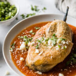 Close-up of a golden brown Mexican chile relleno topped with red salsa on a white plate.