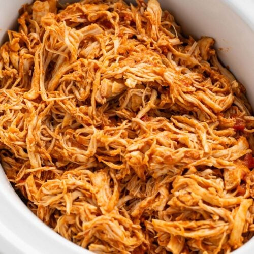 Square image of shredded Mexican chicken in a white slow cooker.