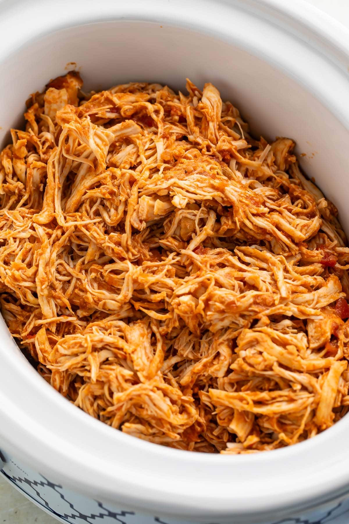 Mexican shredded chicken in a white slow cooker on a kitchen counter.