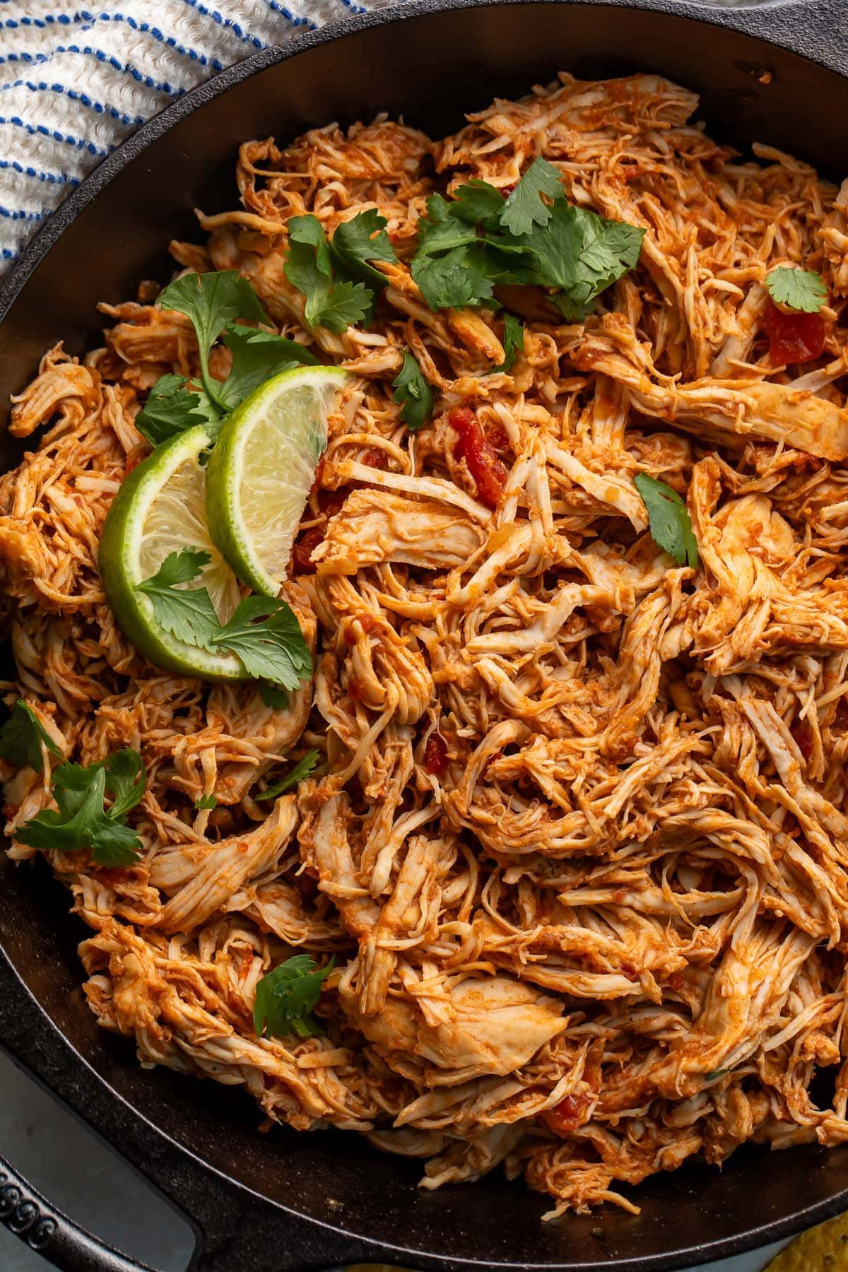 Close-up of shredded Mexican chicken with cilantro and lime in a cast iron skillet.
