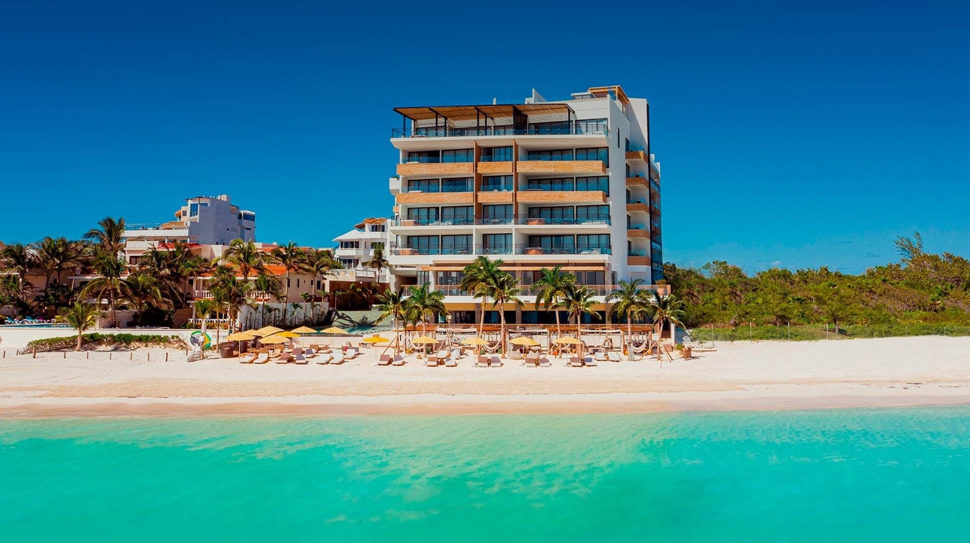 alt= Beachfront view of a Cancun hotel with lounge chairs and umbrellas.