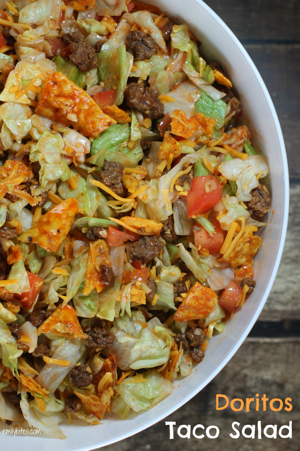 Close-up shot of Doritos Taco Salad in a clear bowl, showcasing layers of lettuce, seasoned ground beef, tomatoes, cheese, Doritos, and dressing.