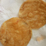 Two tortillas draining excess oil on paper towels.