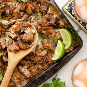 A featured image of crispy carnitas on a baking sheet, garnished with lime wedges.
