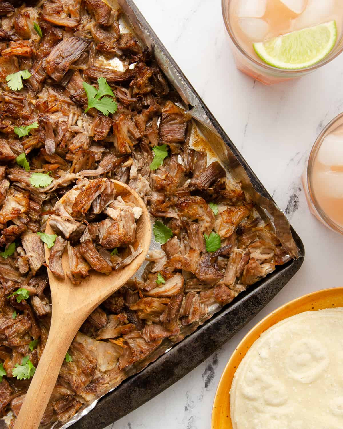 Crispy carnitas on a baking sheet, garnished with lime wedges.