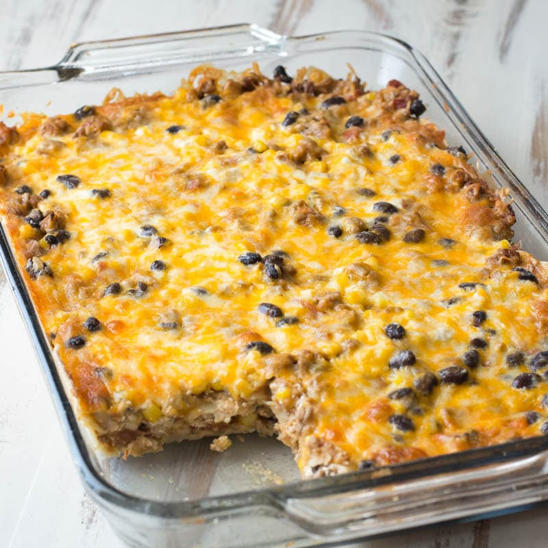 Image showing a pan of freshly baked mexican taco lasagna with tortillas, with a serving spoon resting in the dish, ready to be served.