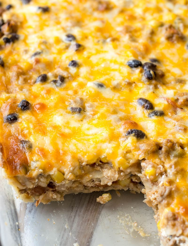 Overhead view of a prepared pan of mexican taco casserole with corn tortillas, with a slice already removed to show the layers inside.