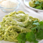 White plate showcasing Mexican Green Spaghetti, topped with cheese and cilantro, highlighting the creamy green sauce and noodle texture