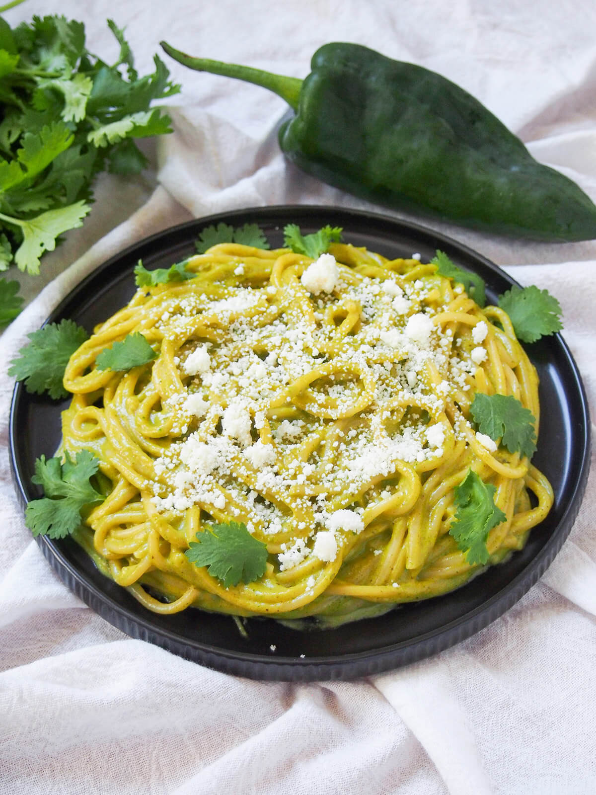 side view of plate of espagueti verde, Mexican green spaghetti with poblano pepper behind