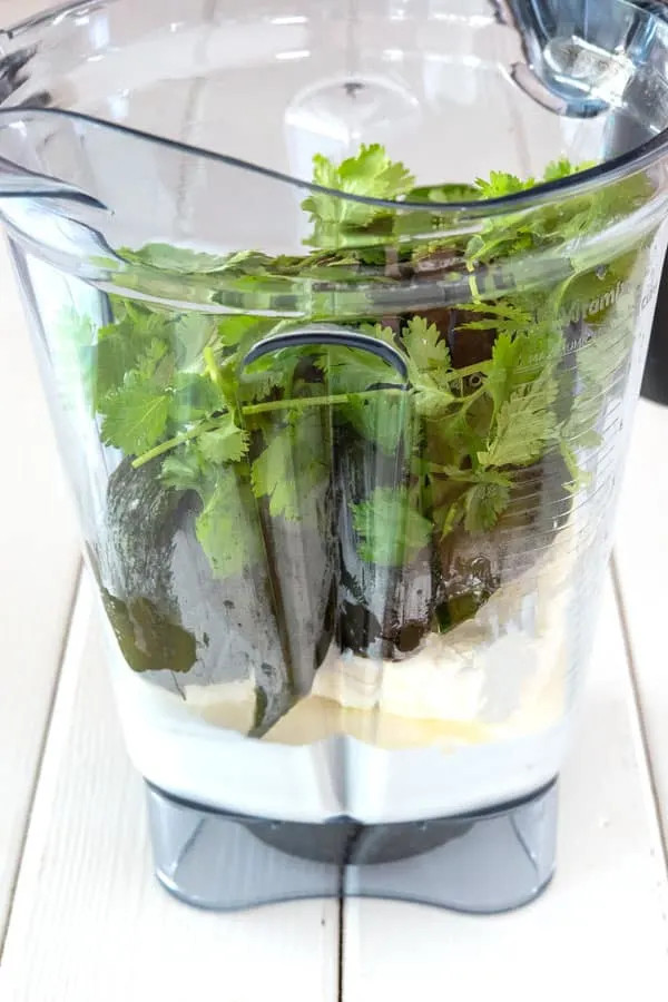 A blender containing the ingredients for Espagueti Verde sauce, ready to be blended into a smooth green sauce