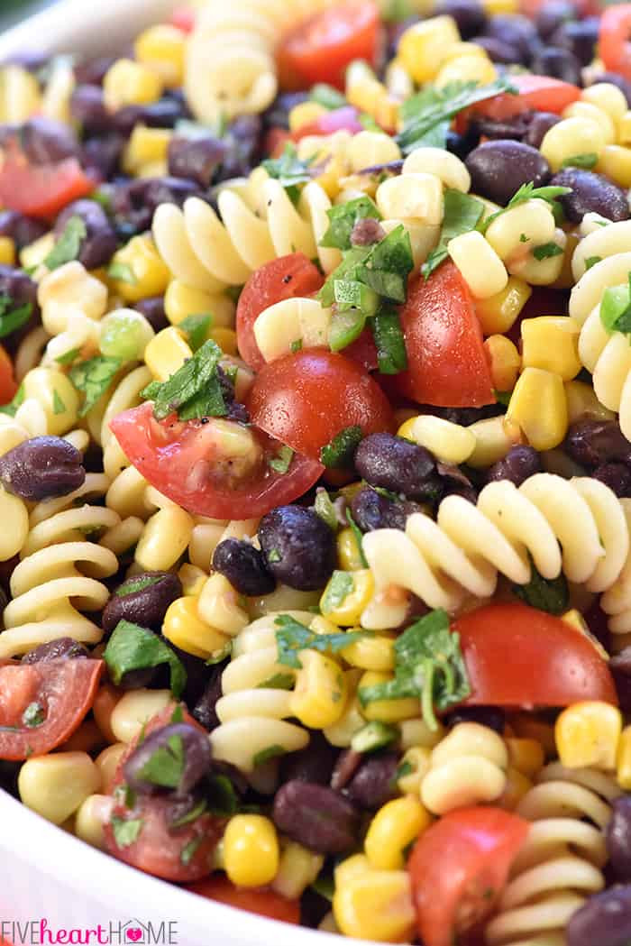 Overhead shot of the fresh ingredients for Mexican Pasta Salad including corn, black beans, tomatoes, jalapeño, and cilantro in separate bowls.