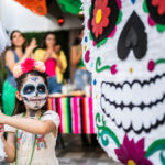 Girl hitting pinata at a celebration in Mexico, showcasing the evolving traditions of Mexican Halloween.