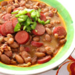 Close-up shot of Frijoles Charros in a clay pot, garnished with cilantro and onions, showcasing the rich texture and vibrant colors of this iconic Mexican dish.