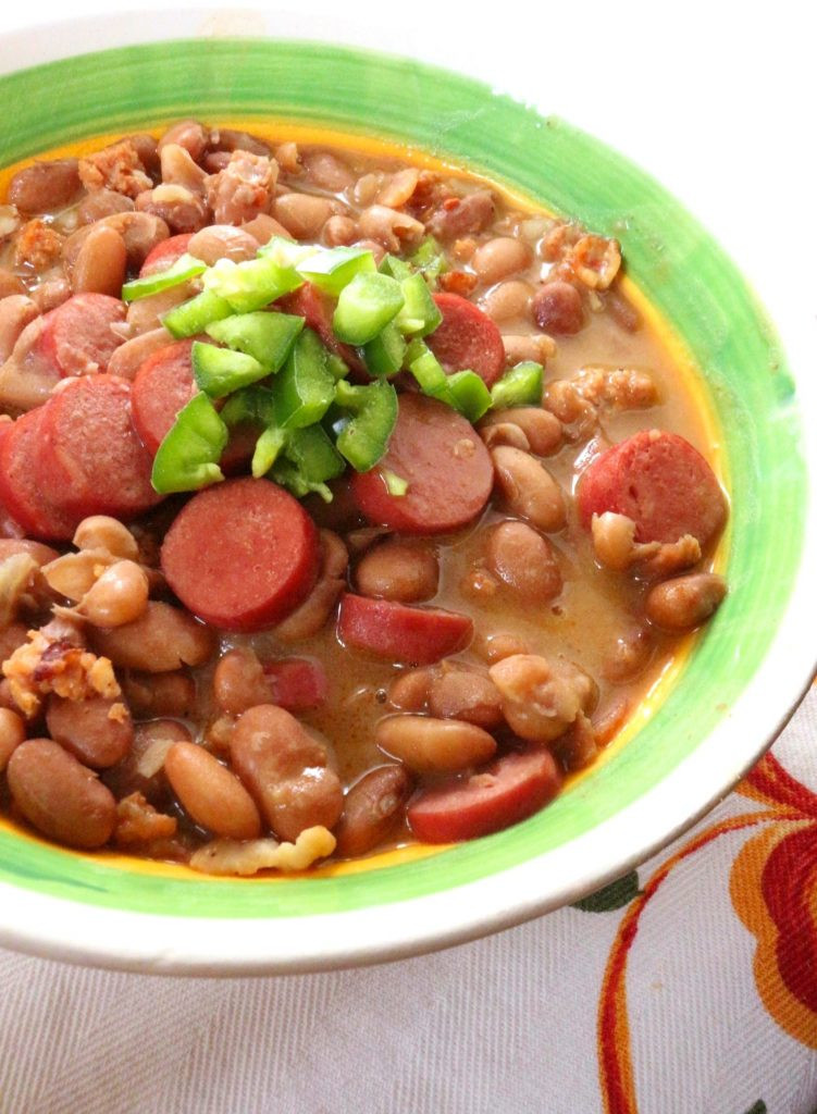 Close-up shot of Frijoles Charros in a clay pot, garnished with cilantro and onions, showcasing the rich texture and vibrant colors of this iconic Mexican dish.