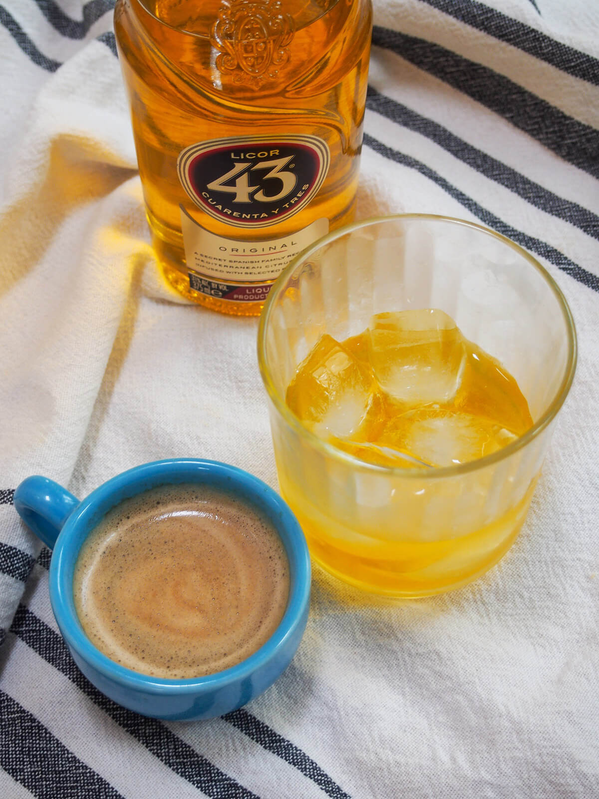 A glass of Licor 43 with a cup of espresso and the bottle behind, highlighting the two main components of the cocktail.