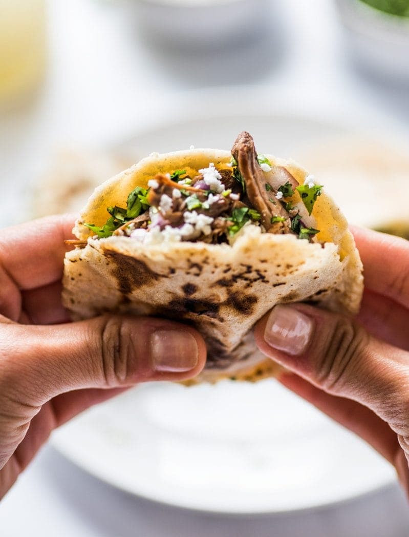 Close-up of a gordita mexican food held in a hand, filled with shredded beef, cheese, and fresh cilantro, showcasing its appetizing texture and vibrant ingredients.