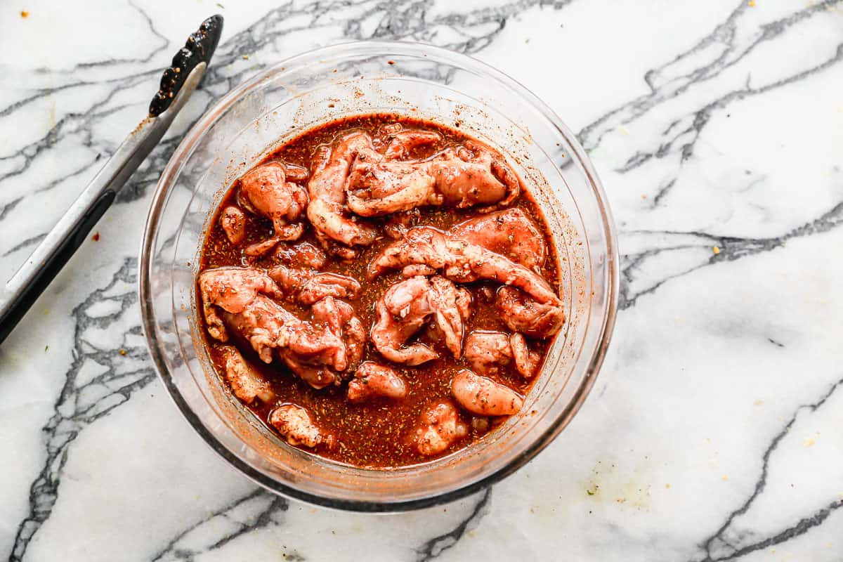 Chicken thighs submerged in marinade in a glass bowl, ready to infuse with flavor for authentic Mexican street tacos.