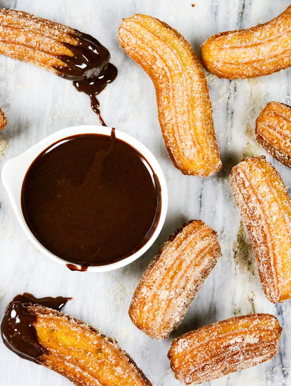 Overhead view of homemade Mexican churros sprinkled with cinnamon sugar and served with a bowl of chocolate ganache, illustrating a complete serving suggestion.