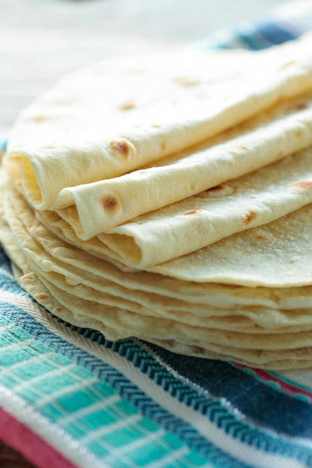 Close-up of a stack of warm homemade Mexican tortillas on a traditional woven cloth.
