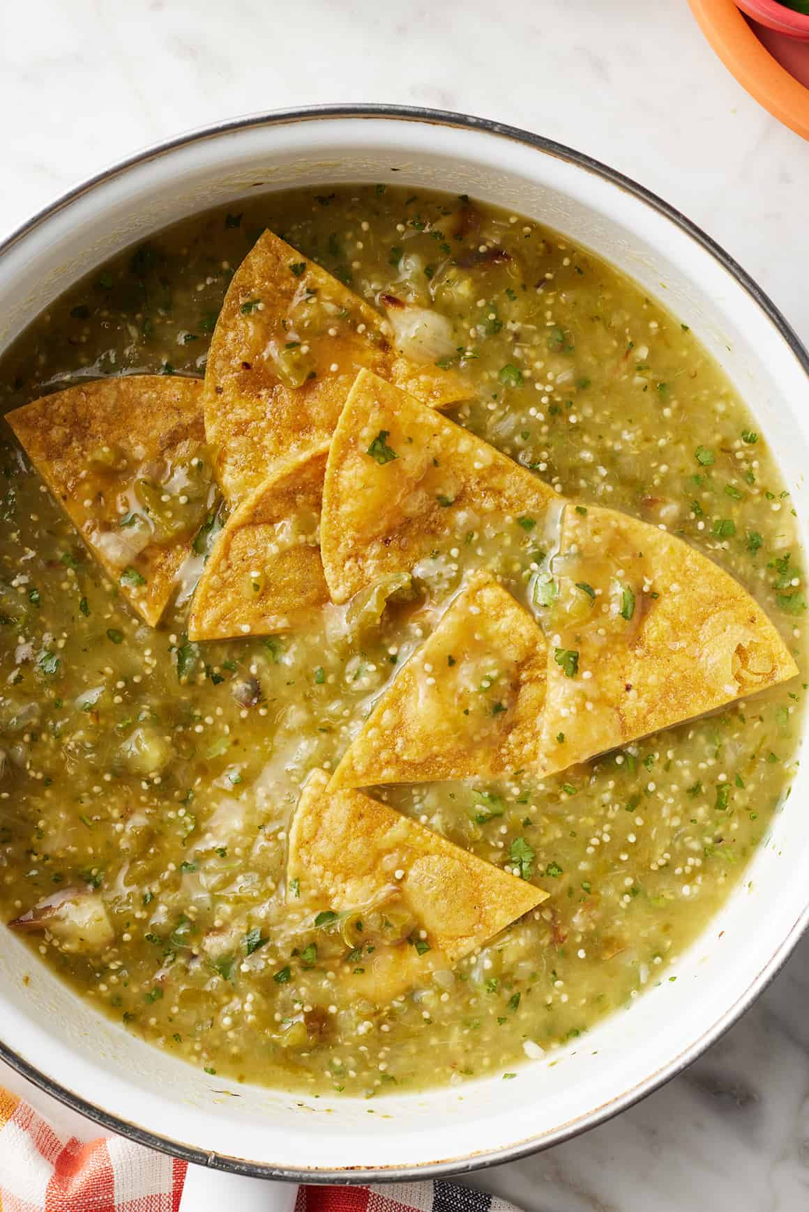 Tortilla chips being added to a skillet with simmering salsa verde.