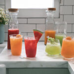 Assortment of Aguas Frescas in glass dispensers, showcasing various fruit colors.