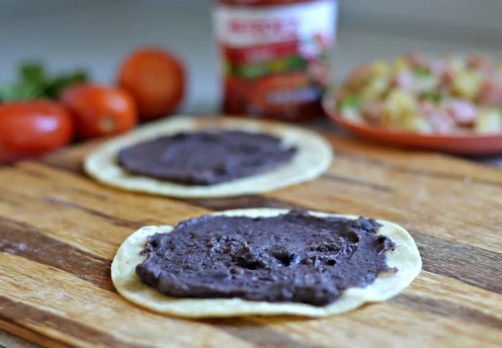 Preparing tortillas and refried beans for Huevos Rancheros, layering the foundation of this classic Mexican breakfast.